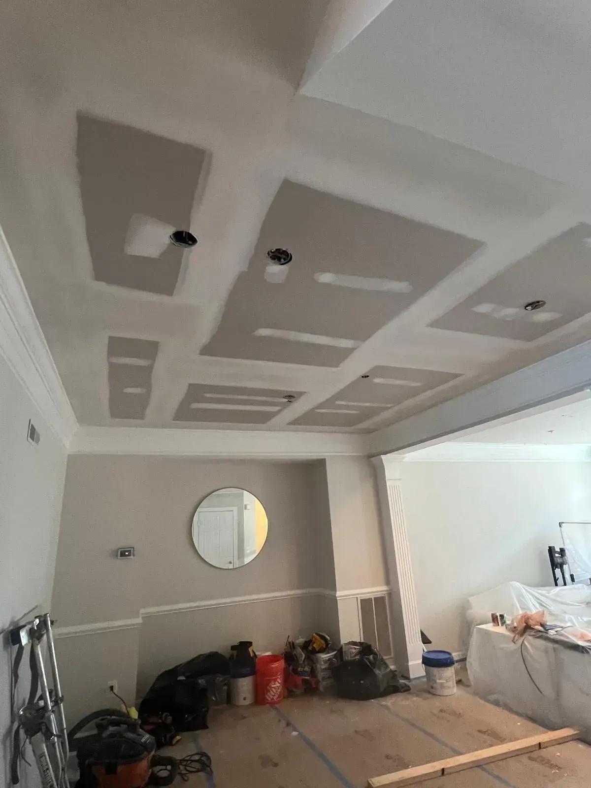 Partially finished room with drywall ceiling patches, round wall mirror, and renovation materials on the floor