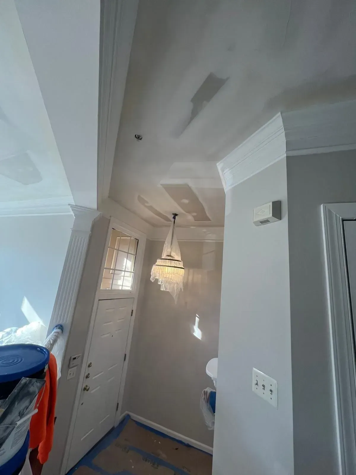 Narrow hallway with a white front door, hanging light fixture, gray walls, and blue floor covering
