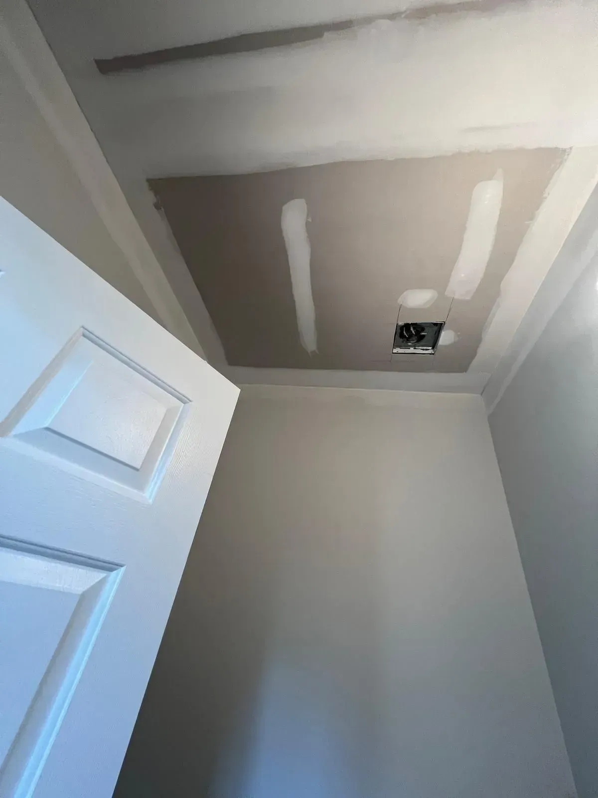 Partially finished ceiling with drywall patches and recessed light opening above a white door