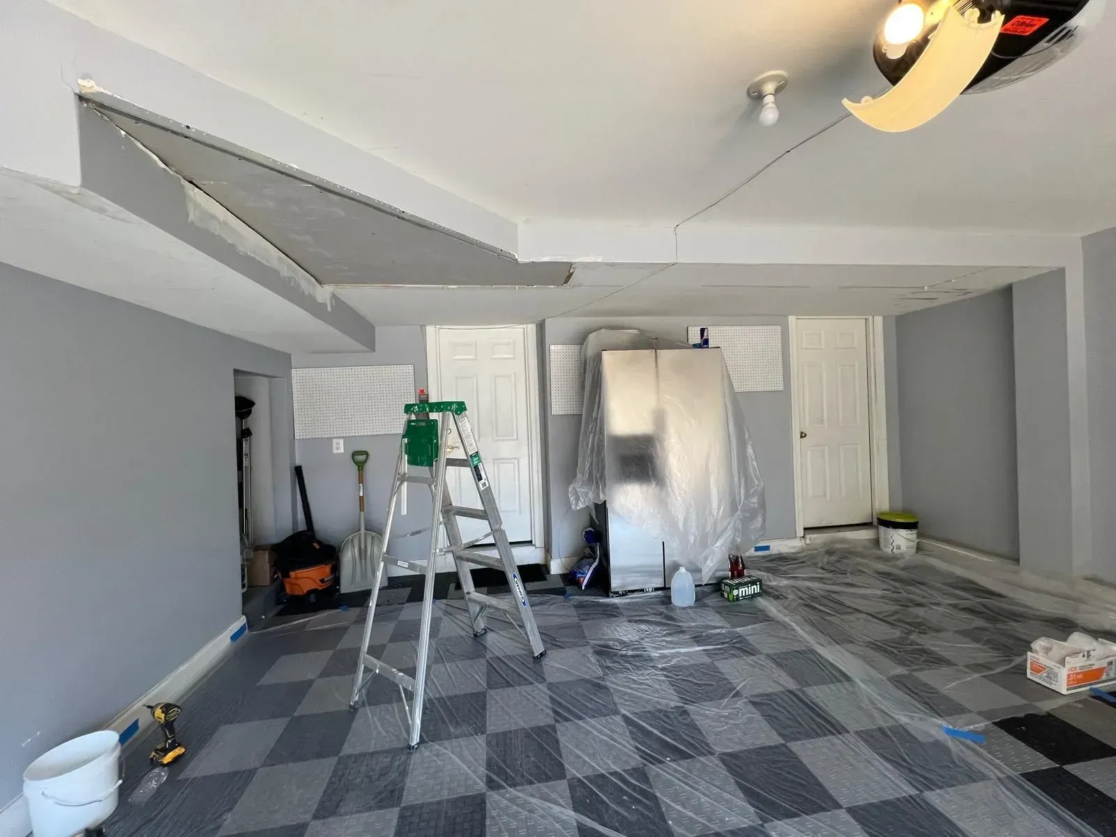 Renovating garage with ladder, paint cans, and covered furniture on a checkered floor