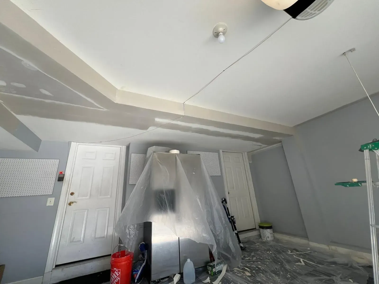 Plastic-covered room under renovation with gray walls, white doors, and scattered drop cloths on the floor