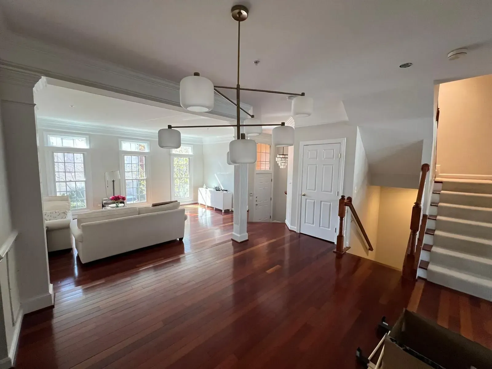 Bright open kitchen and living area with red wood floors, white cabinets, and staircase at right