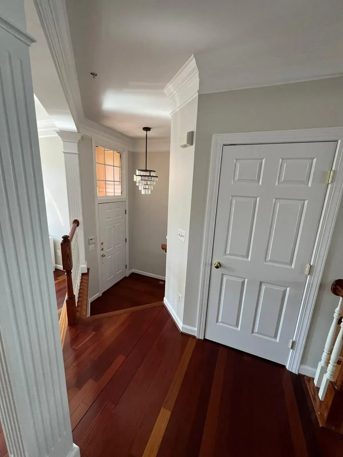 Hallway with hardwood floors, white doors, and a hanging light fixture.