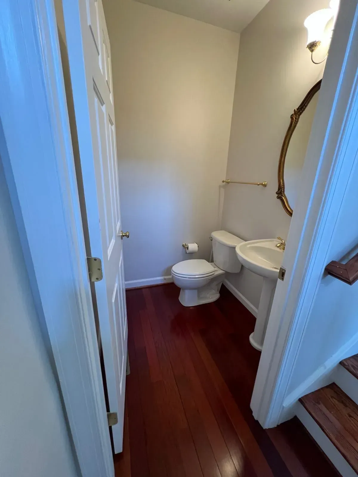 Small bathroom with toilet, sink, and red floor viewed through a doorway
