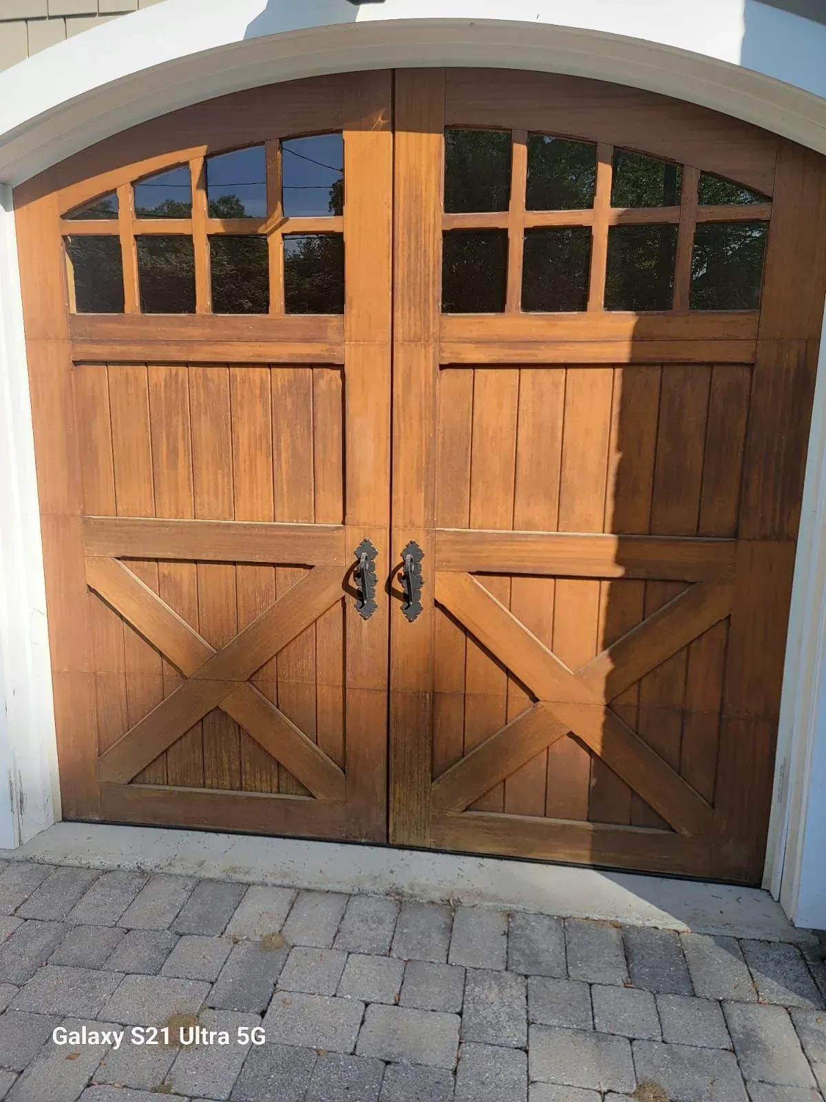 Closed wooden double garage doors with arched windows on a stone driveway