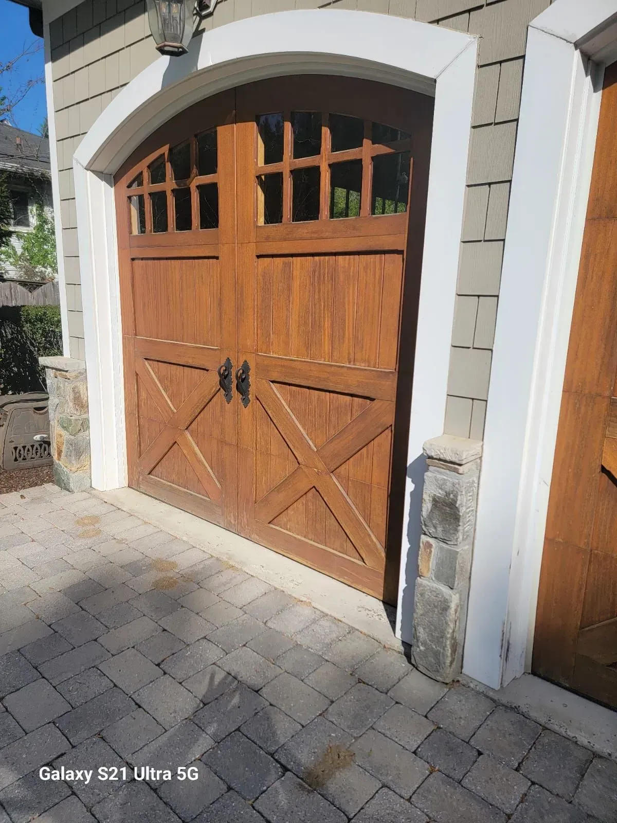 Wooden garage door with arched white stone trim and cobblestone driveway in front