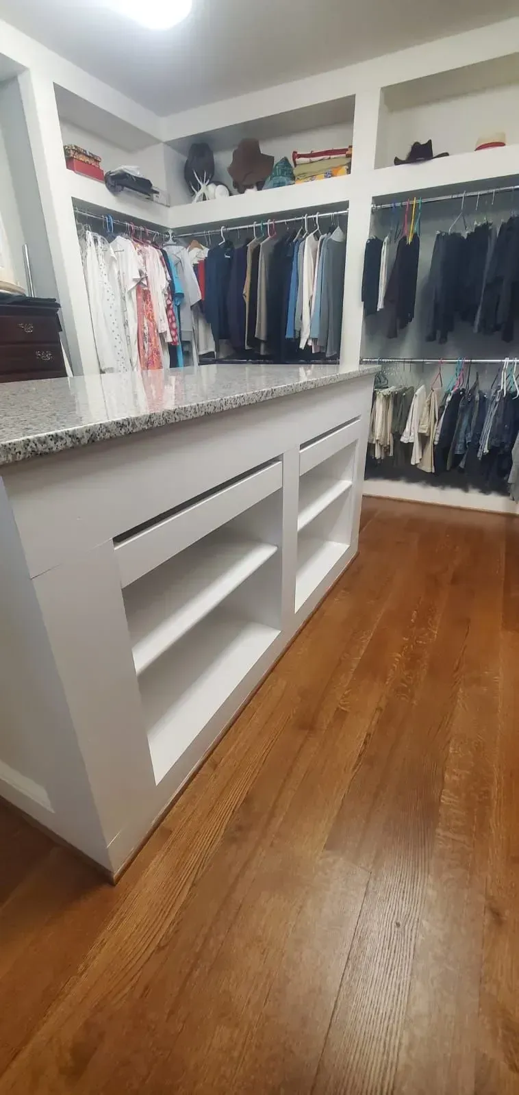 Walk-in closet with white built-in shelves, hanging clothes, and a wooden floor.