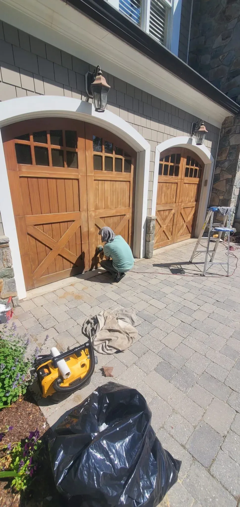 Two wooden garage doors with an arched stone facade; a person in green kneels near the left door.