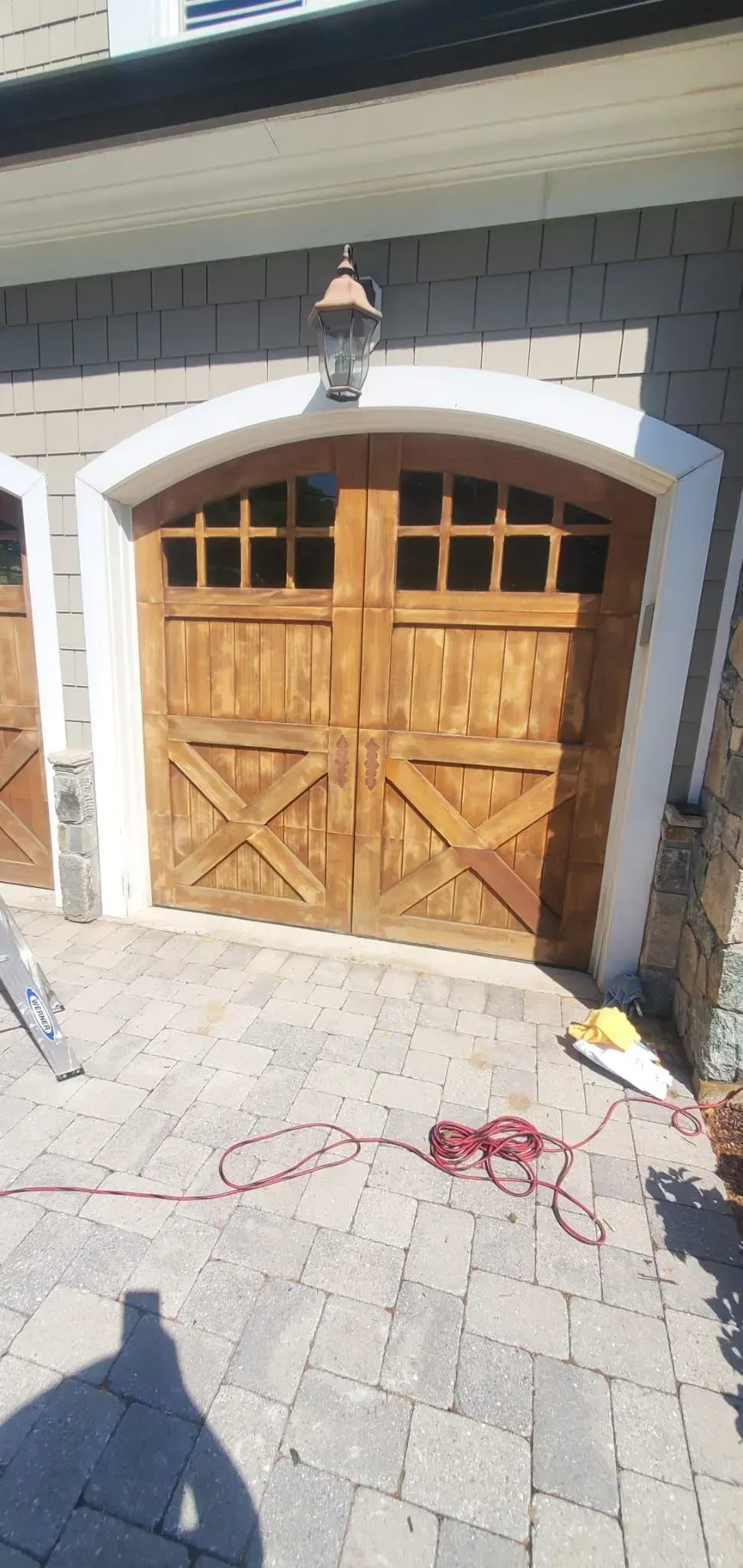 Wooden garage door with white trim under a lantern on a stone driveway.