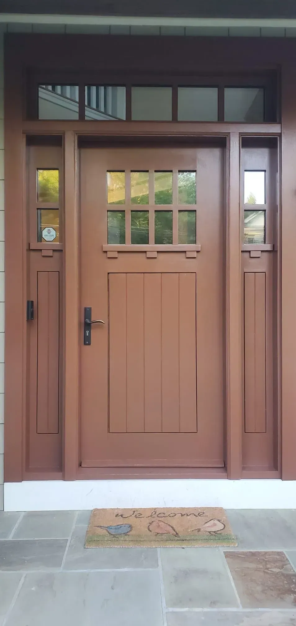 Front entrance with a brown wooden door, glass panes, and a welcome mat under a covered porch