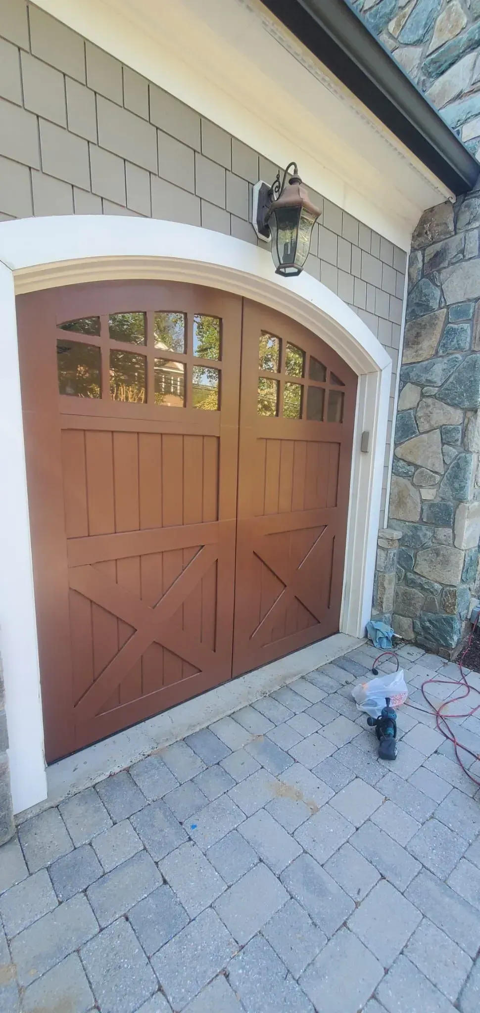 Wooden double garage door set in a stone-and-stucco house exterior with a small front walkway.