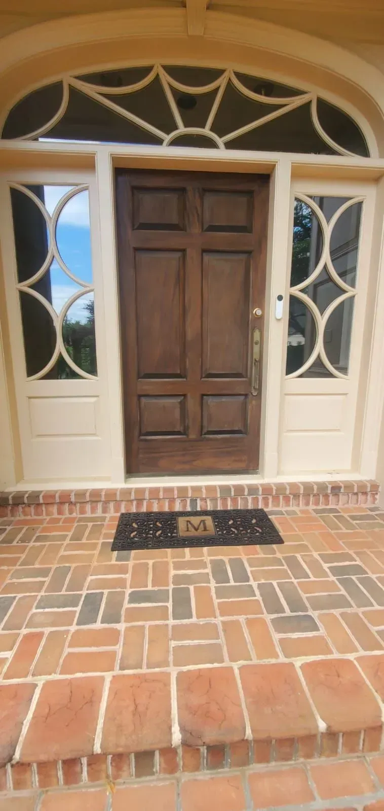 Front entrance with a wooden door, decorative glass sidelights, and brick steps leading up to it