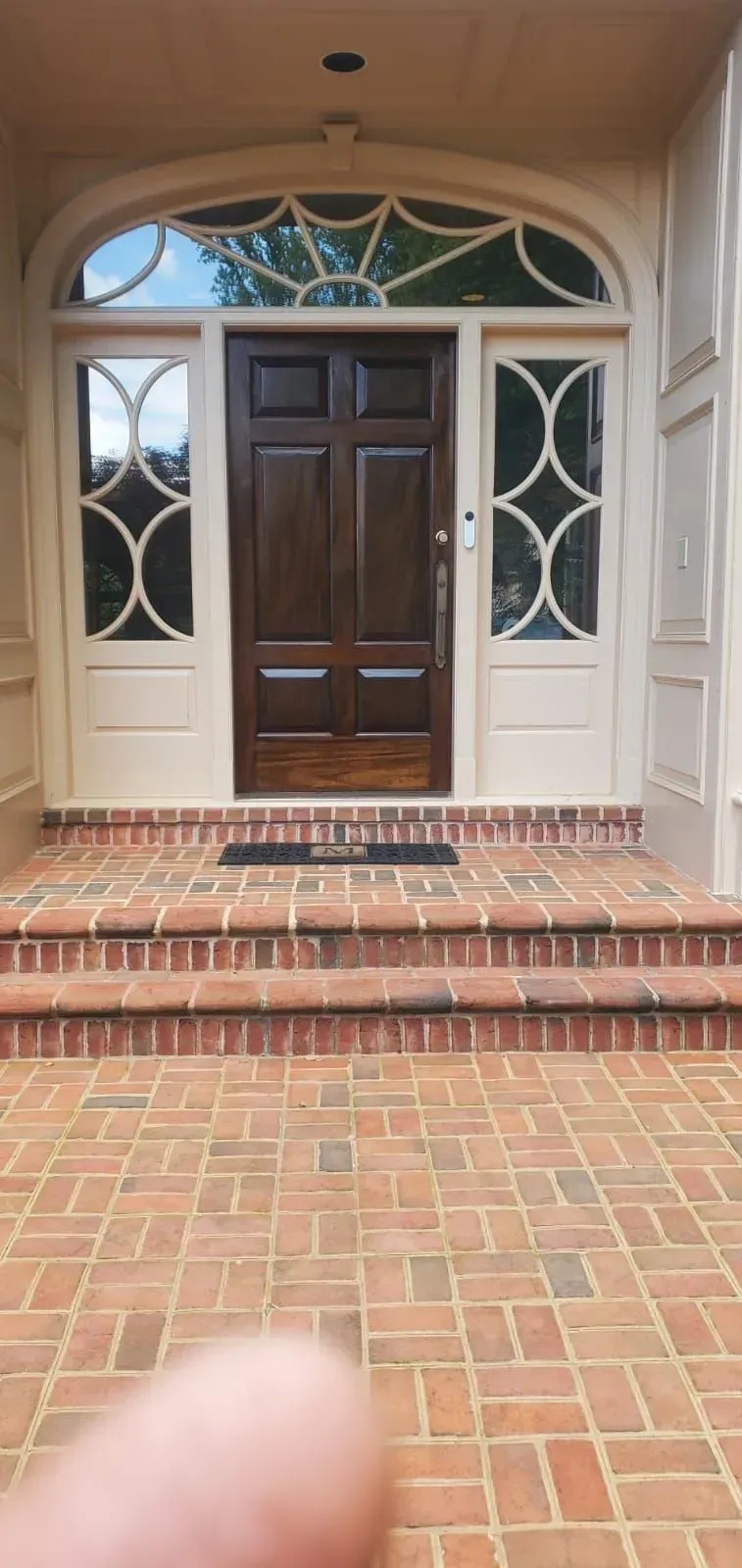 Brick porch with steps leading to a dark wooden front door and side windows with decorative glass