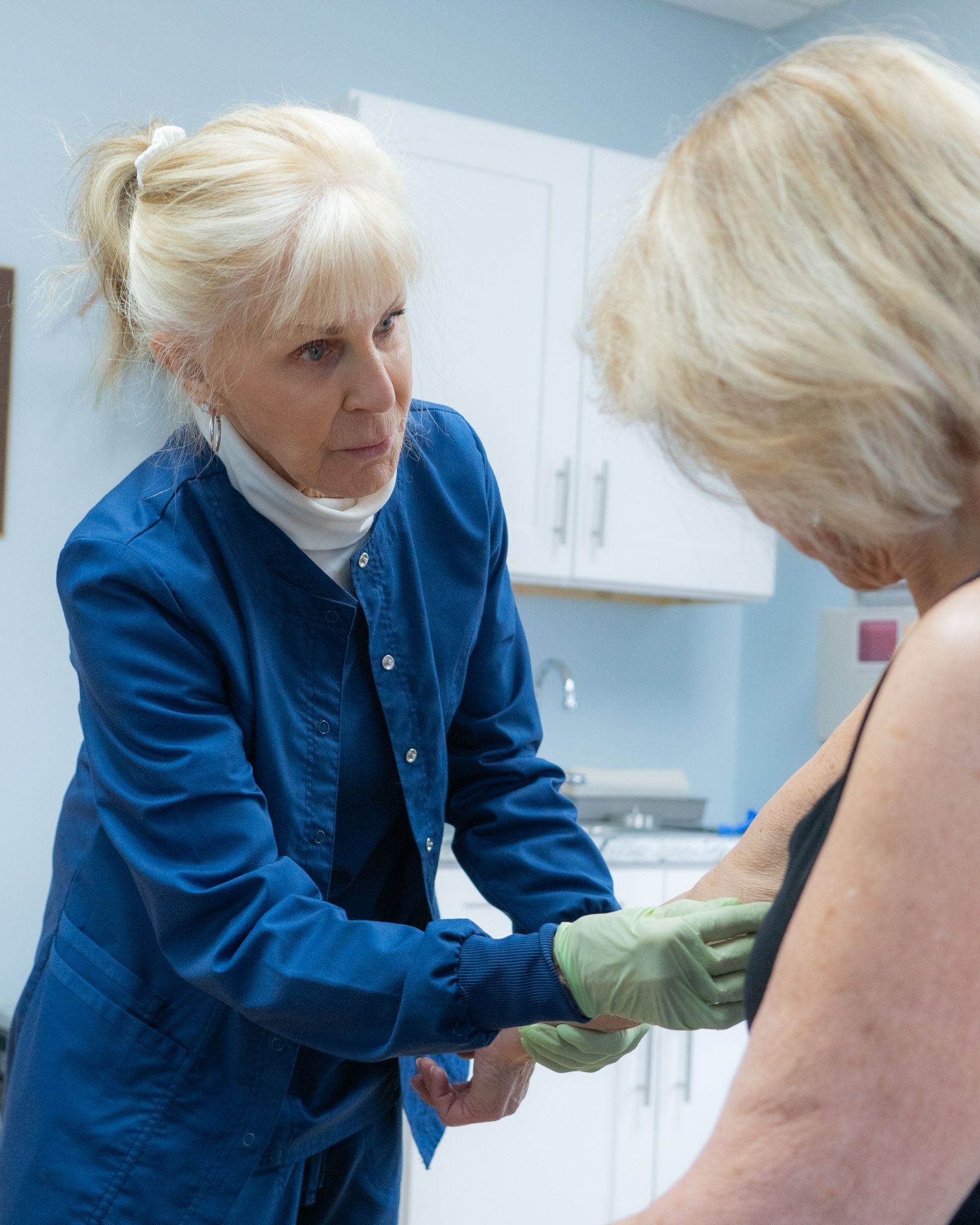 Woman in blue scrubs tending to another woman's arm in a medical setting.