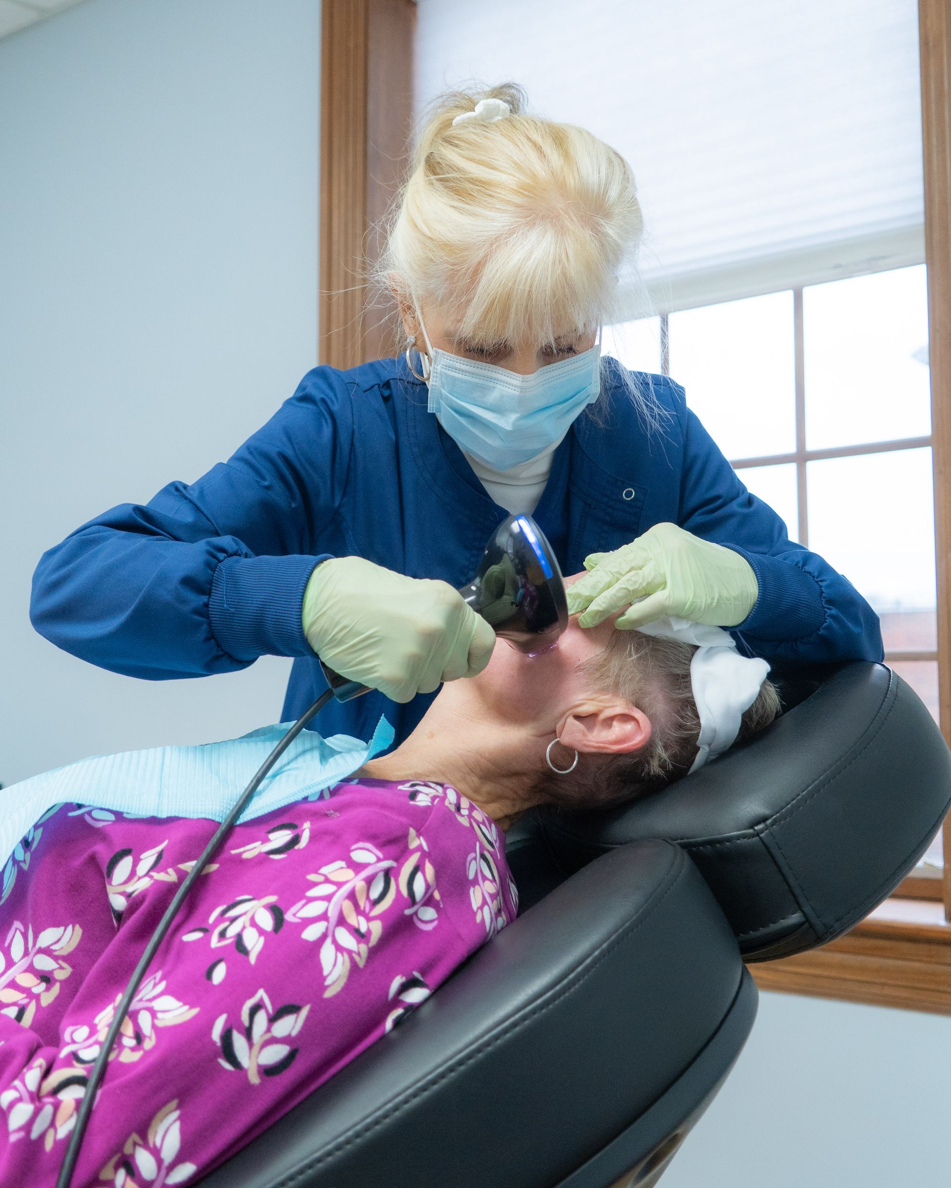 Dental assistant placing oxygen mask on patient in dental chair.