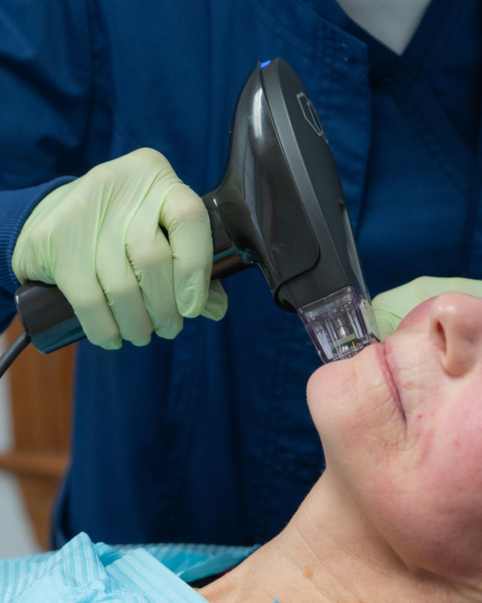 Person receiving a facial treatment with a handheld device; gloved hands, blue scrubs.