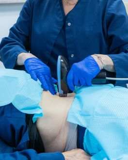 Person in blue scrubs and gloves administering a medical procedure, possibly a neck ultrasound.