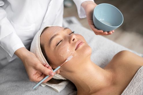 Woman receiving facial treatment in a spa, with a mask being applied by a professional.