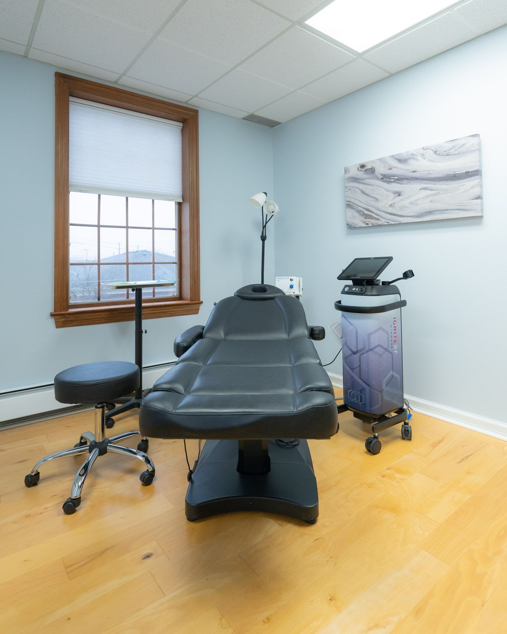 Medical examination room with black chair, equipment, and window.