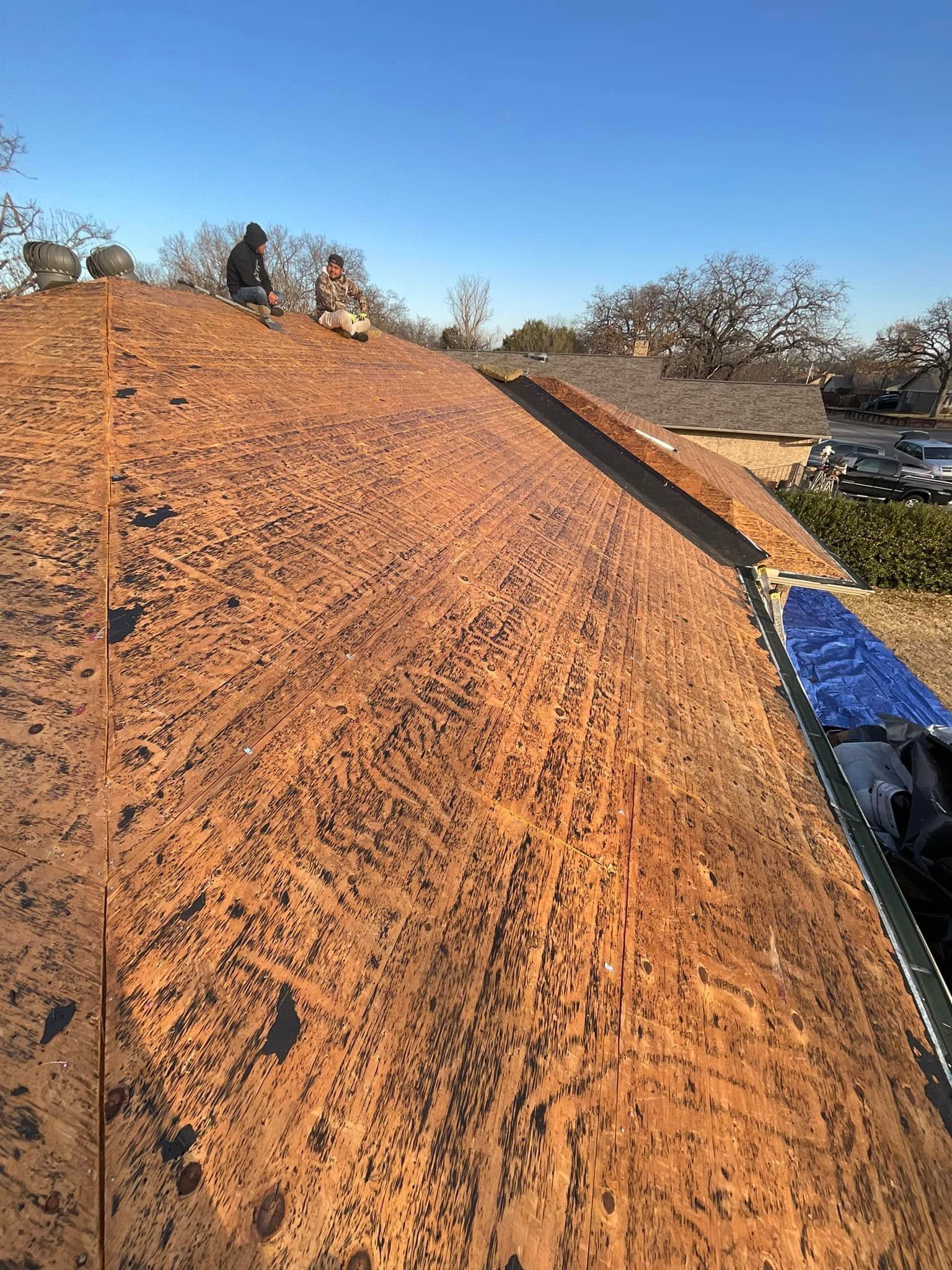 Orange dirt-covered roof under construction with a ladder along the edge and trees in the background