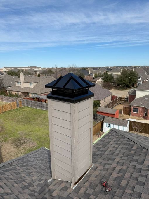 Suburban rooftop chimney with black cap under a clear blue sky, overlooking nearby houses and yards