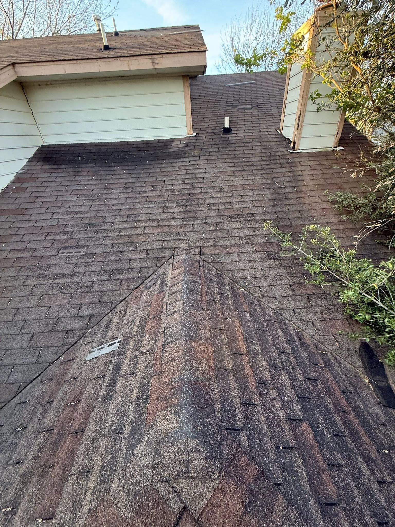 Steep shingled roof with visible ridge damage beside a white house and chimney