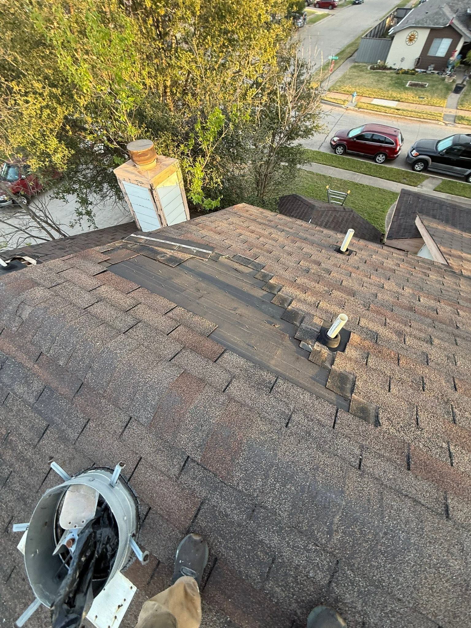Rooftop with weathered shingles, skylight, vent fan, and trees and parked cars below