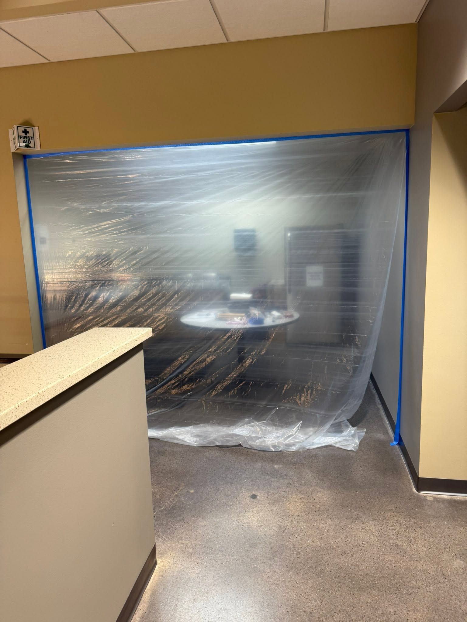 Office hallway blocked by clear plastic sheeting, with beige walls and a counter in the foreground