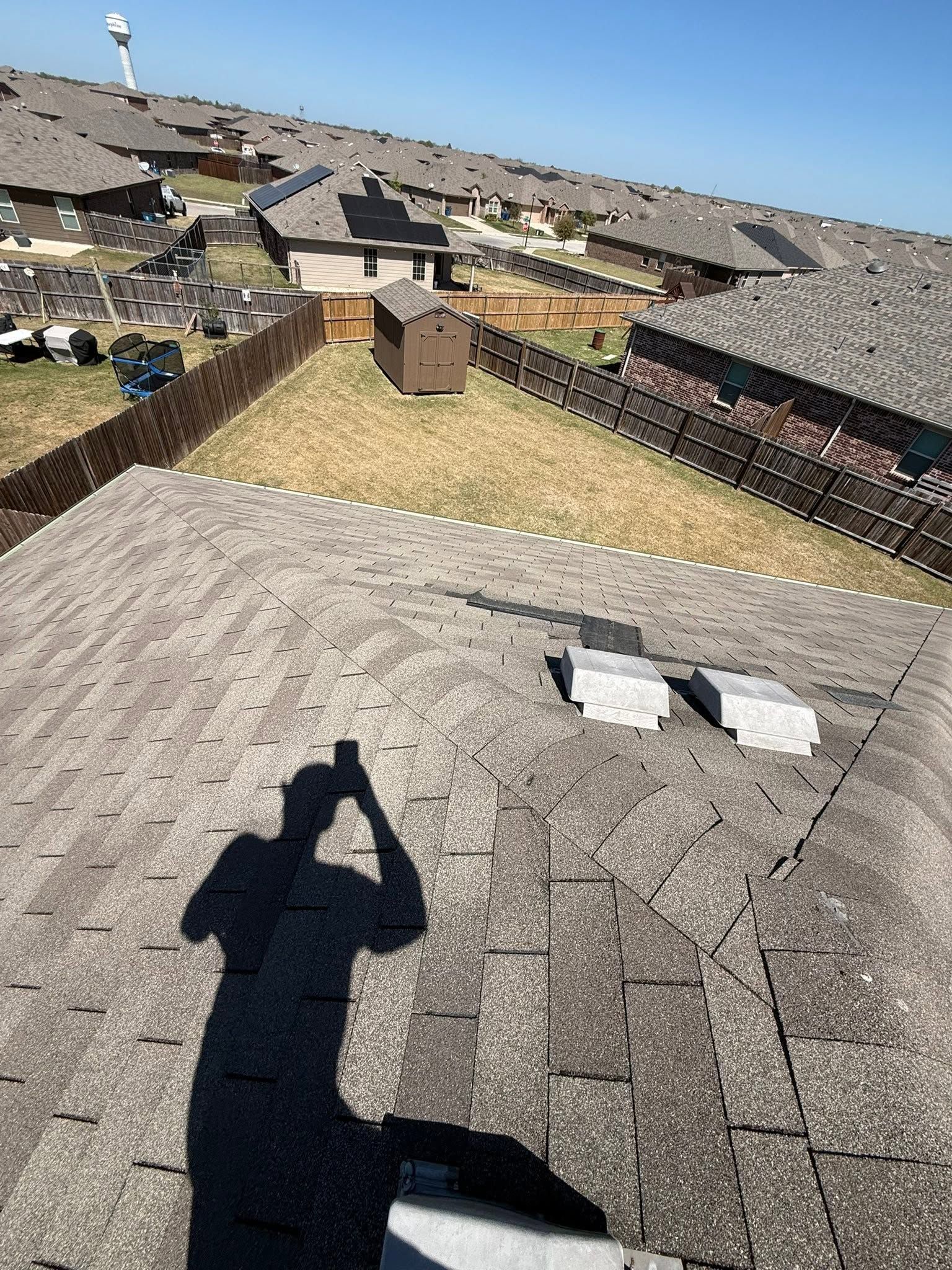 Rooftop view of shingle roofs, skylights, and a person’s shadow taking the photo