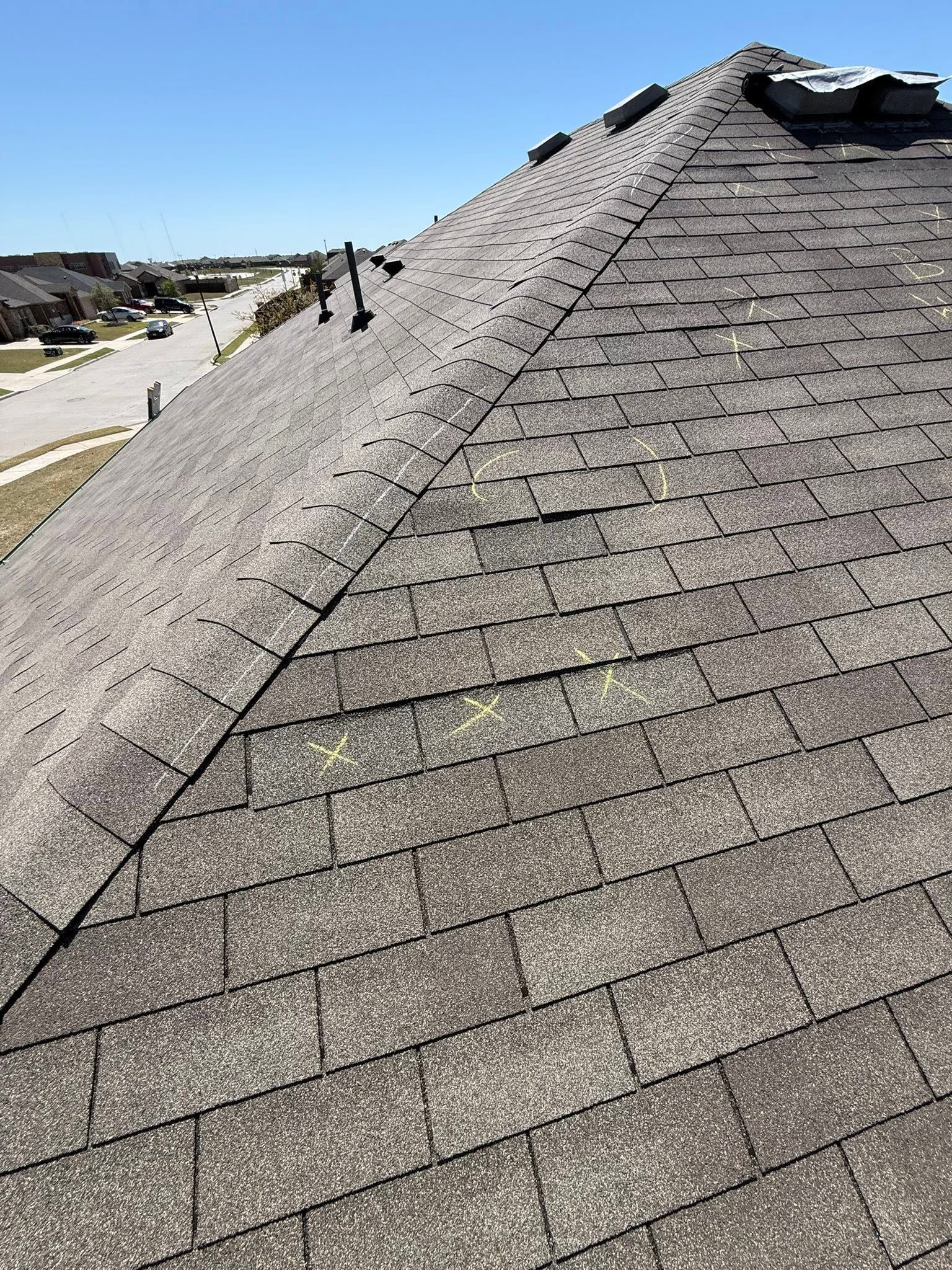 Steep shingled roof under construction with two workers and a cloudy sky