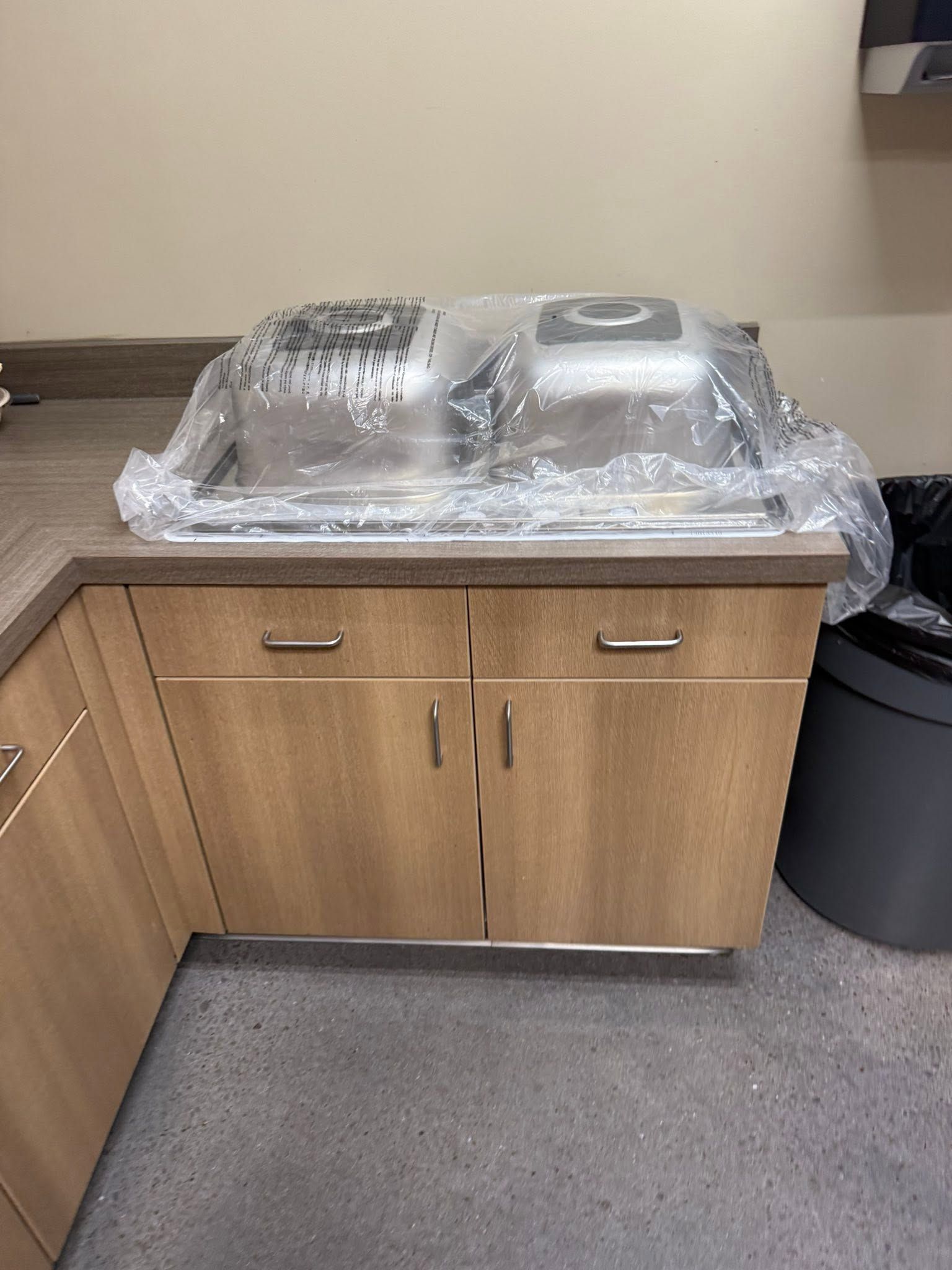 Countertop with covered stainless steel food trays on a wooden cabinet in a break room.