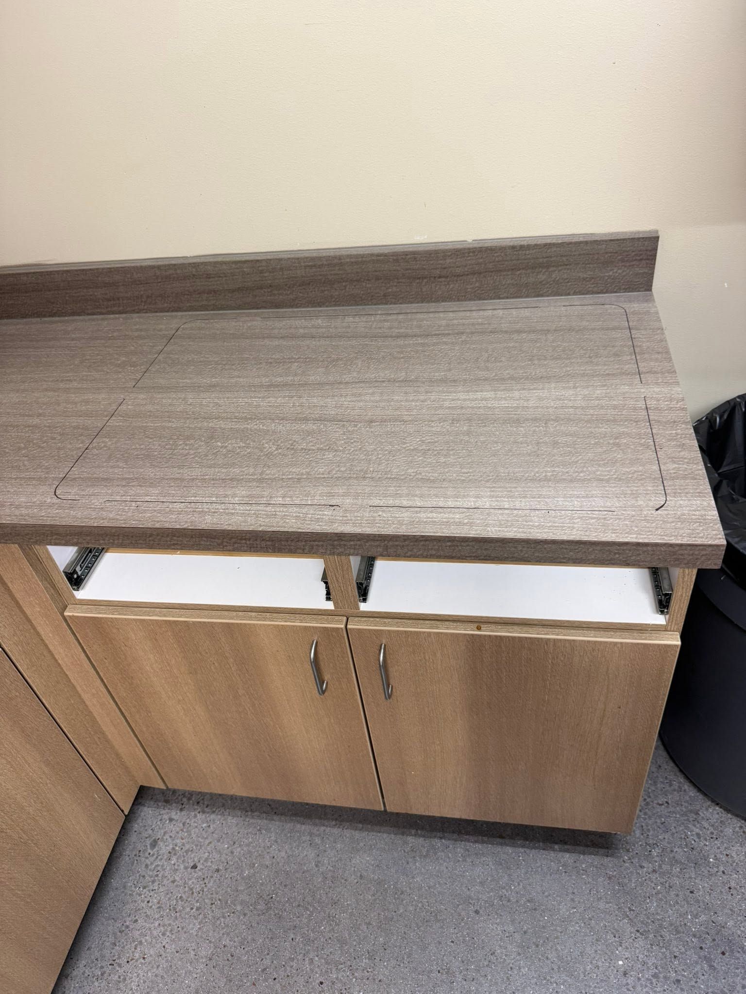 A wooden cabinet with a gray, textured top panel, set against a beige wall on a carpeted floor.