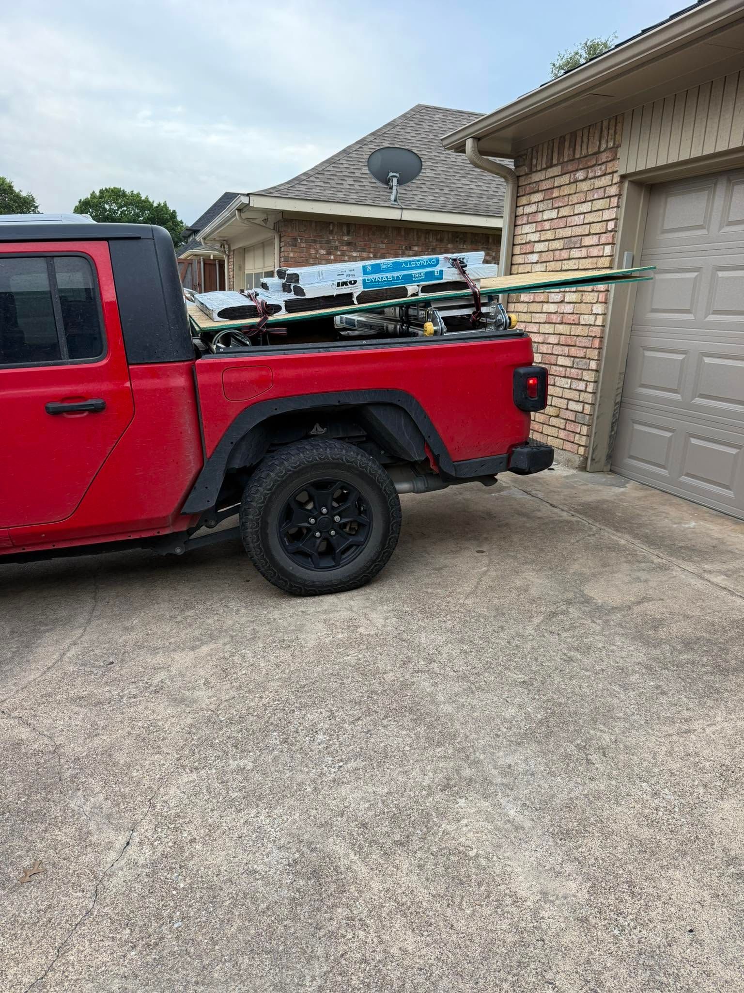 Red pickup truck parked beside a garage, with ladders strapped in the bed.