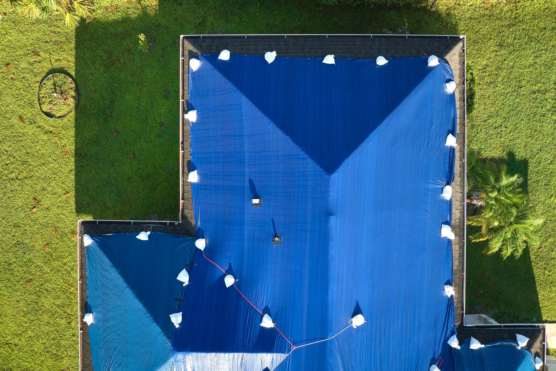 Aerial view of blue-roofed buildings on a grassy lot with white tents around the edges.