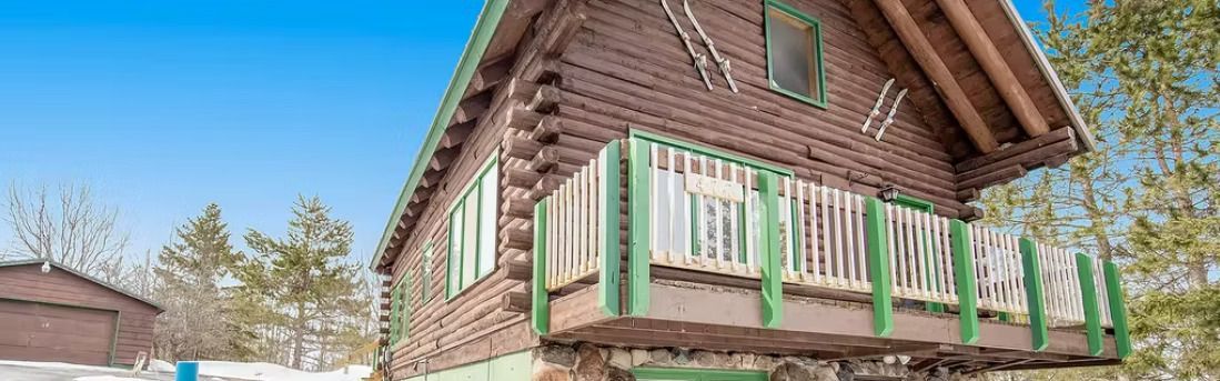 Snowy wooden house with green-trimmed porch and steep roof under a clear sky