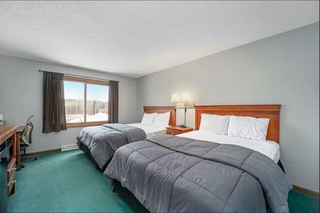 Motel room with two double beds, teal carpet, and a window showing mountains.