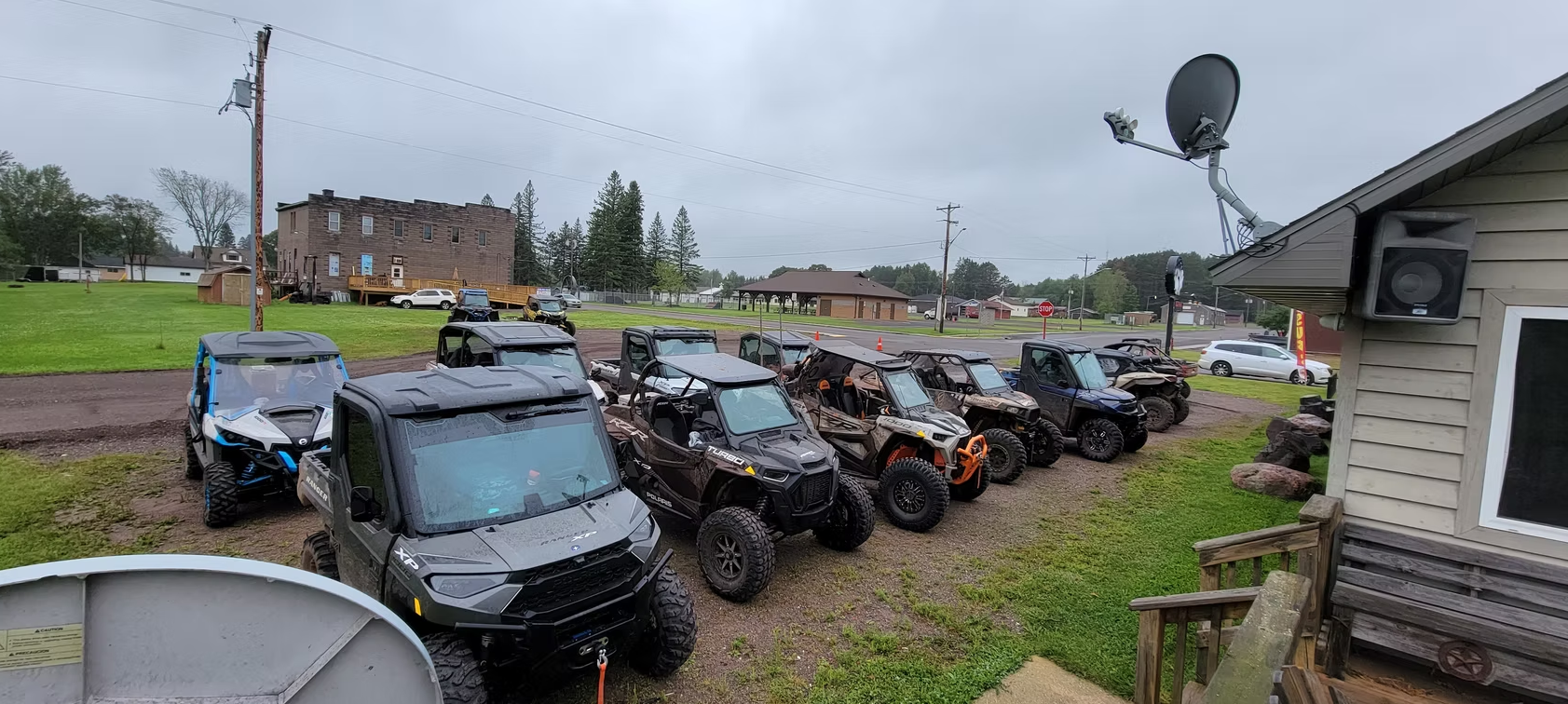Row of parked motorcycles and scooters beside a house in a muddy yard under cloudy skies