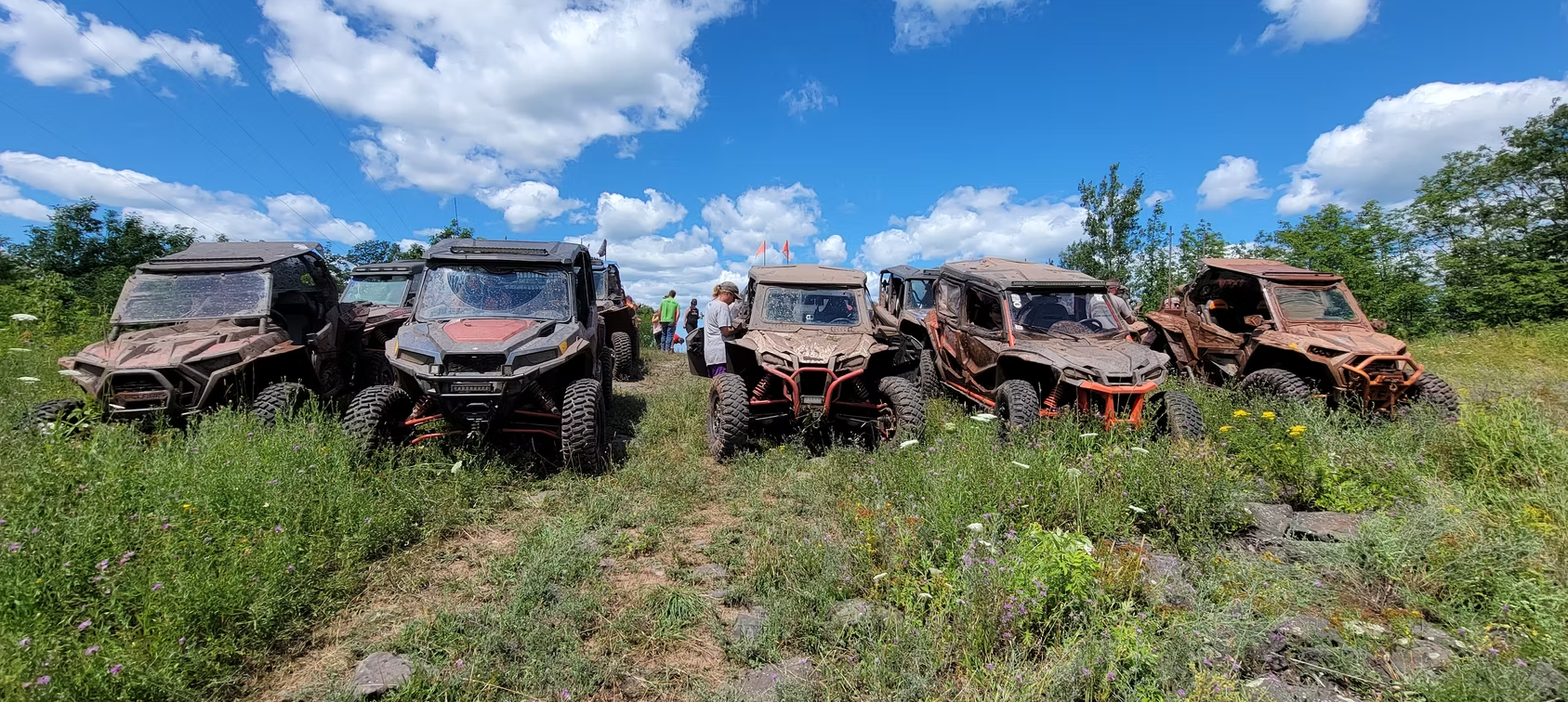 Row of rusty, damaged off-road vehicles in a grassy field under a blue sky