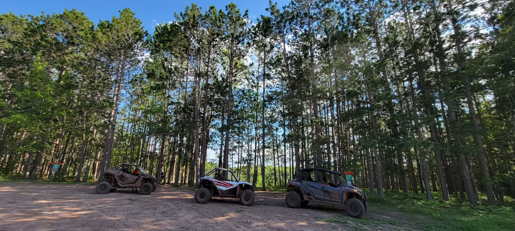Two parked off-road vehicles under tall trees in a wooded clearing