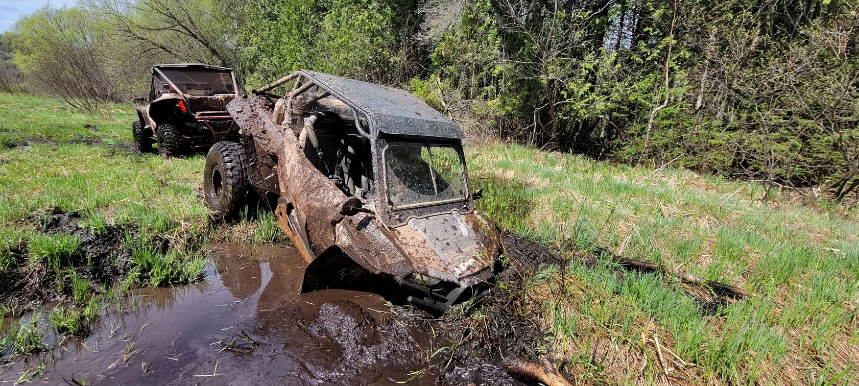 Mud-covered off-road vehicle stuck in a swampy field with trees in the background