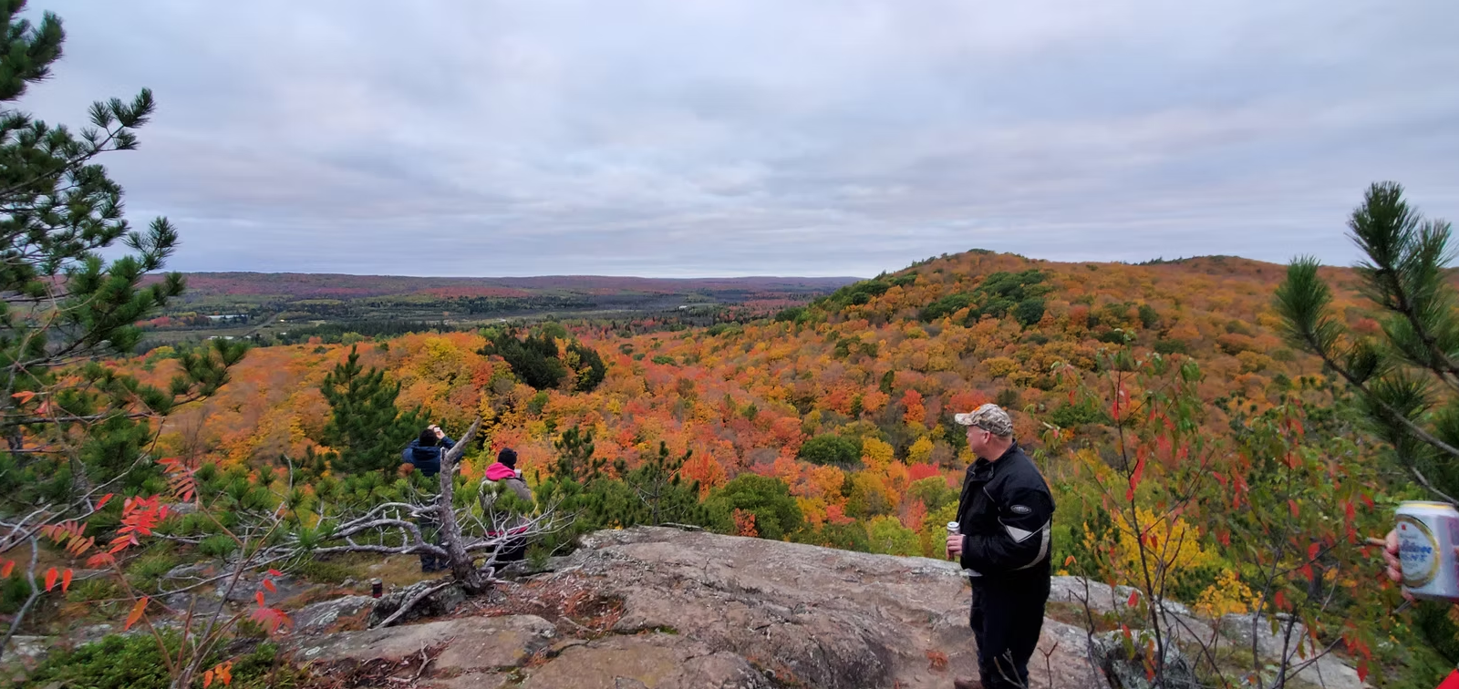 Autumn forest overlook with hikers on a rocky cliff under a cloudy sky
