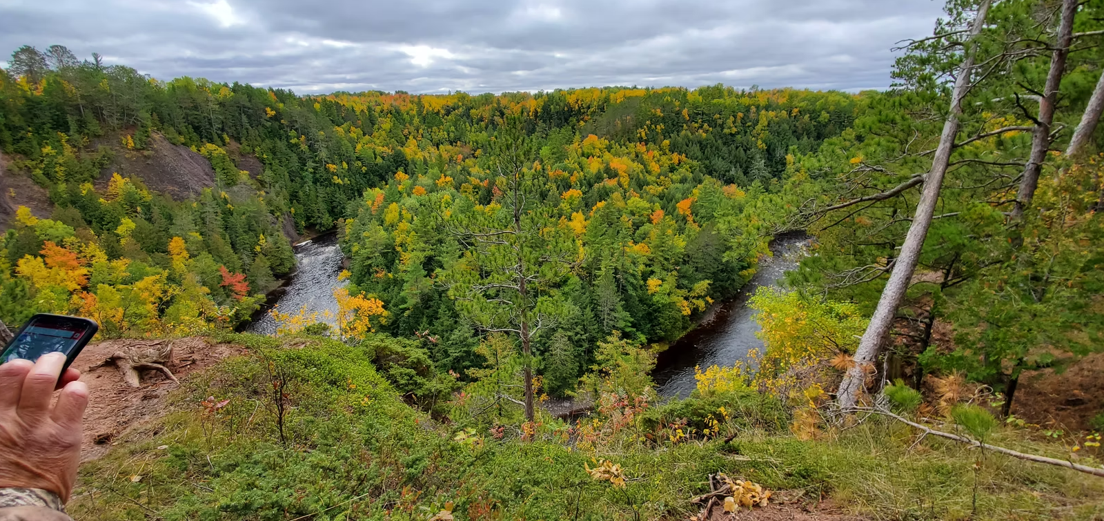 Rugged green valley with autumn foliage and a small stream under a cloudy sky