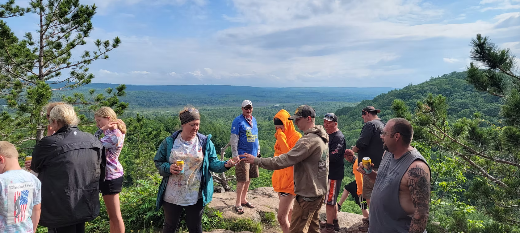 People gathered outdoors in a vineyard, sharing fruit with hills in the background.