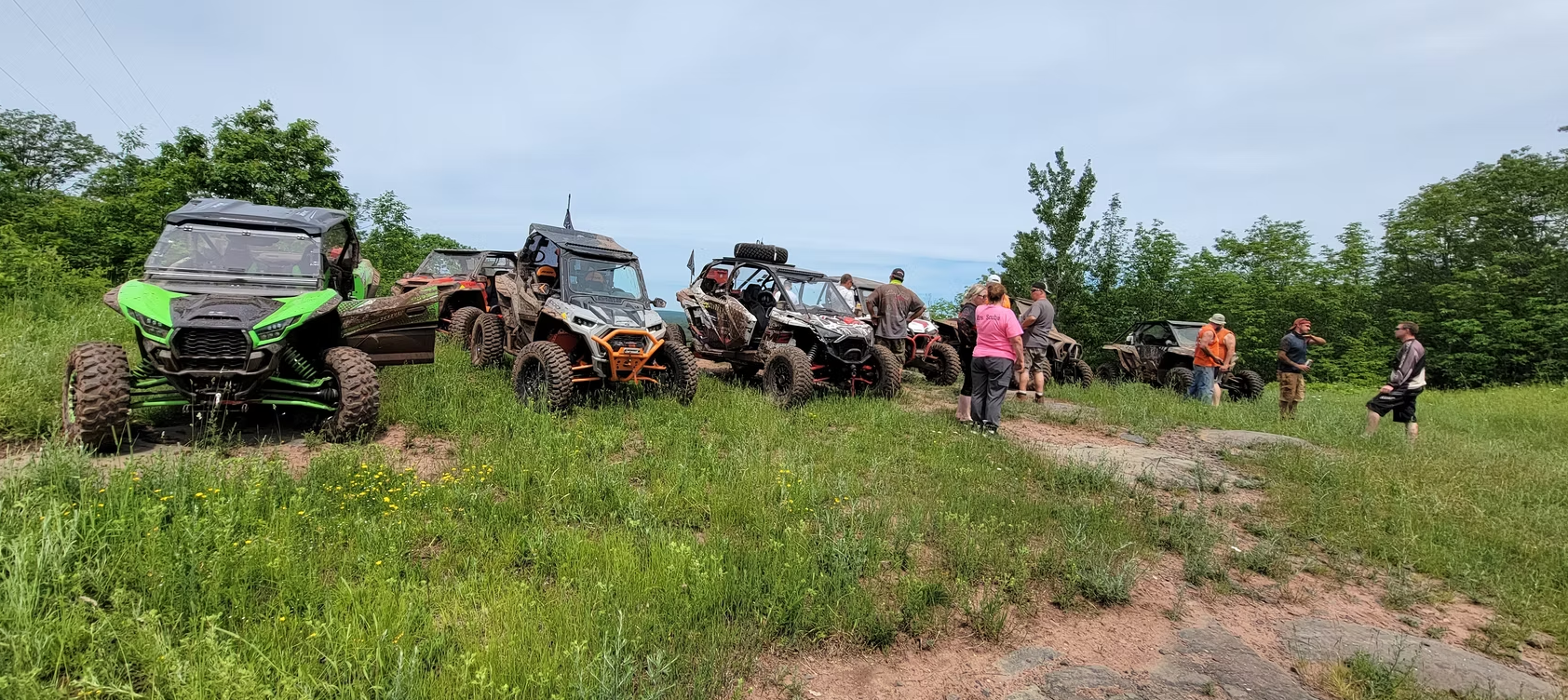Off-road vehicles and people gathered on a grassy trail under a blue sky