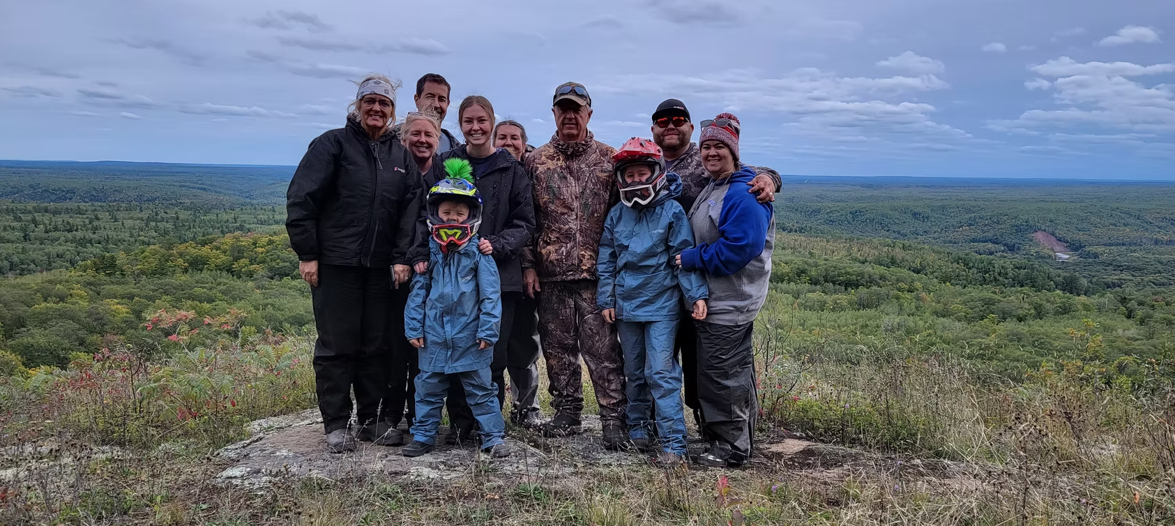 Group of hikers posing on a rocky hilltop with a wide green landscape under a cloudy sky.