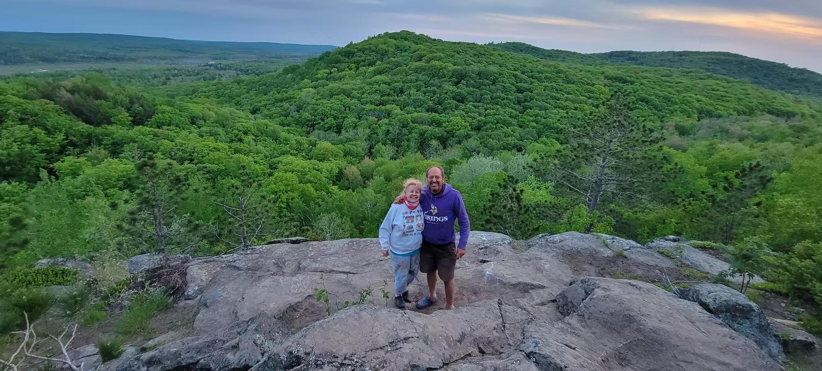 Two hikers standing on a rocky overlook above a lush green forest