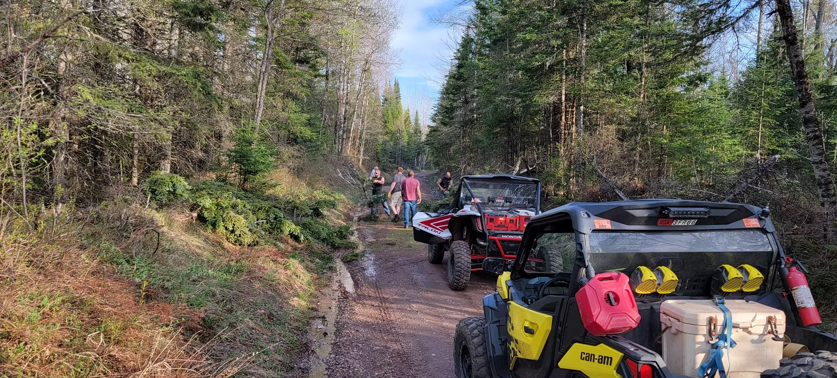 Off-road vehicles lined up on a muddy forest trail with dense trees on both sides