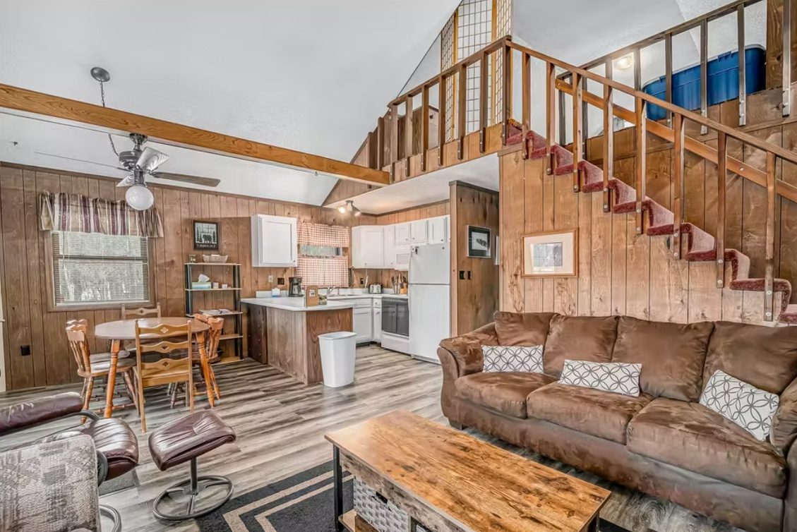 Cozy cabin living room with wood stove, loft stairs, and brown sectional sofa