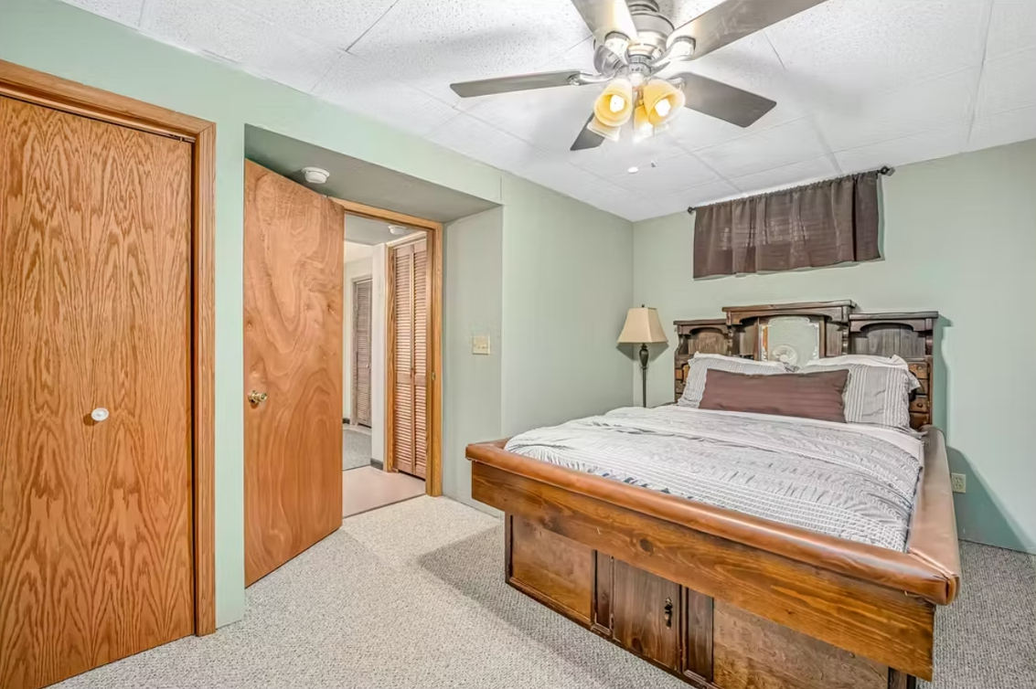 Bedroom with wood bed, ceiling fan, closet doors, and light green walls
