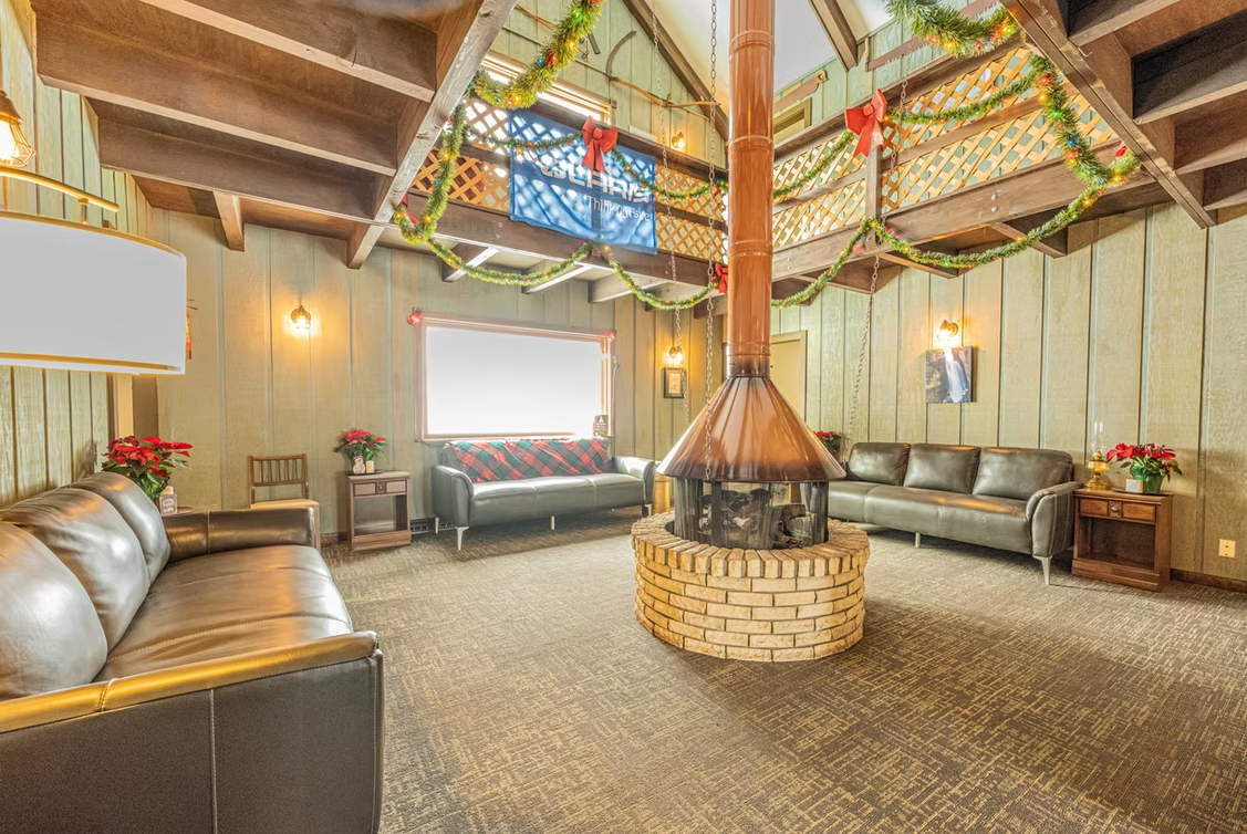 Rustic living room with leather sofas, stone fireplace, high wood beam ceiling, and colorful stained-glass window